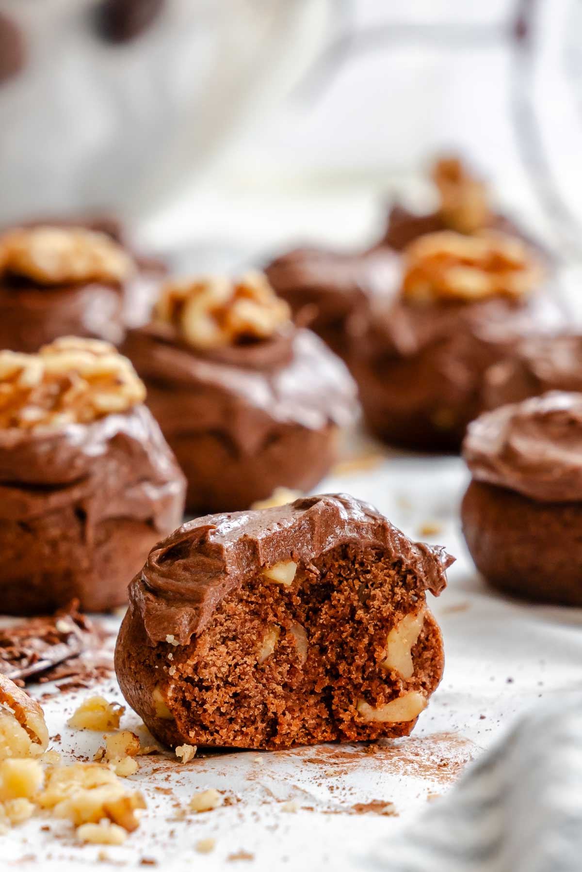 A bitten chocolate spice cookie showing the soft center with chopped walnuts, surrounded by other frosted cookies.