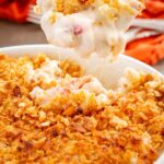 A close up of a spoon lifting a creamy scoop of lobster mac with a crunchy Ritz cracker topping from the casserole dish.