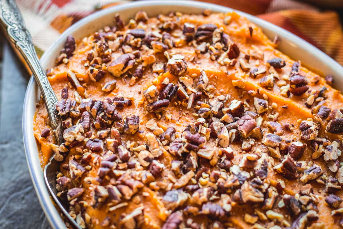 Close-up of creamy orange sweet potato mash topped with toasted chopped pecans in a white oval casserole dish.