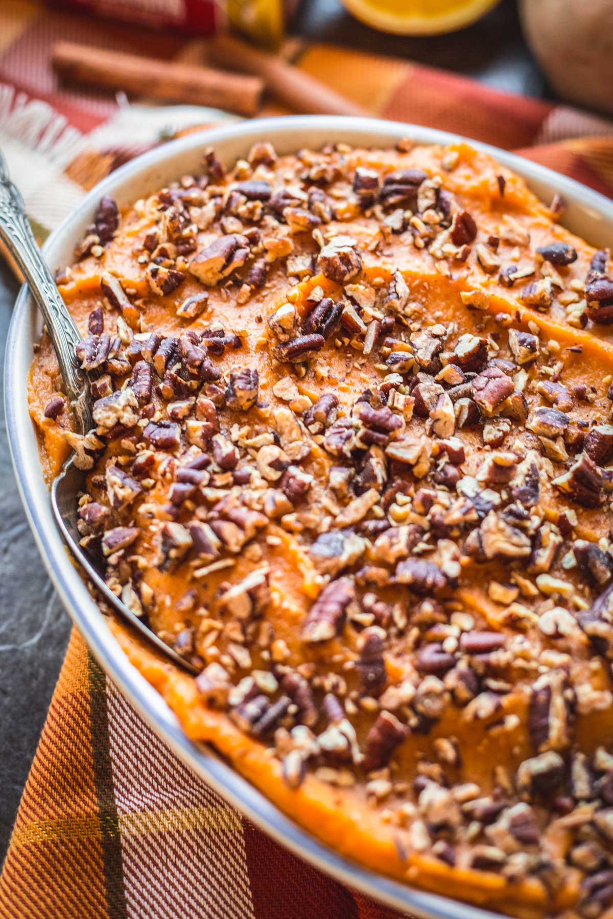 Overhead view of sweet potatoes with brown butter and pecans served in an oval baking dish with a silver serving spoon.