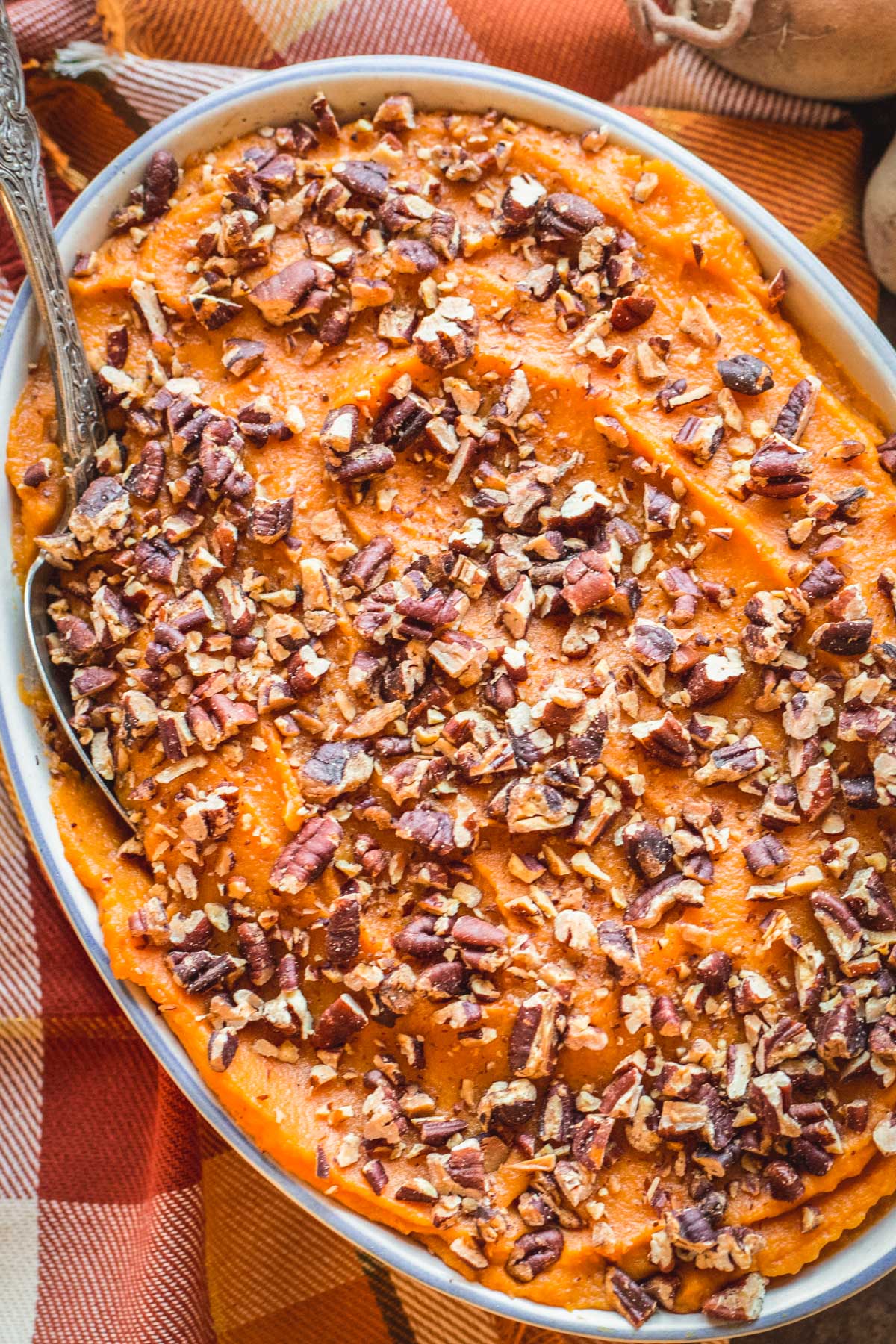 Top-down image of smooth sweet potato casserole garnished with crunchy toasted pecans on a plaid fall tablecloth.