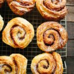 Freshly baked morning buns cooling on a wire rack, coated with a dusting of sugar and showing defined laminated layers.