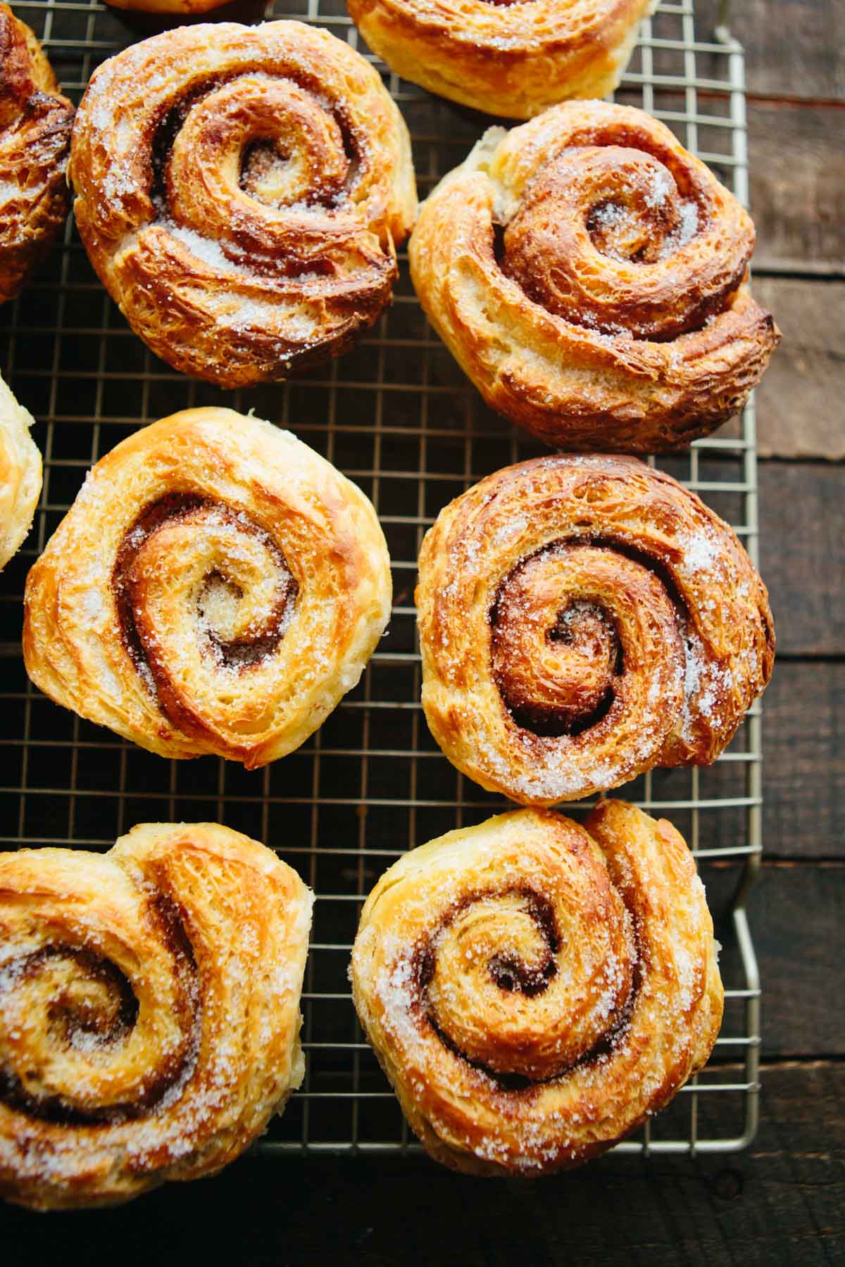 Freshly baked morning buns cooling on a wire rack, coated with a dusting of sugar and showing defined laminated layers.
