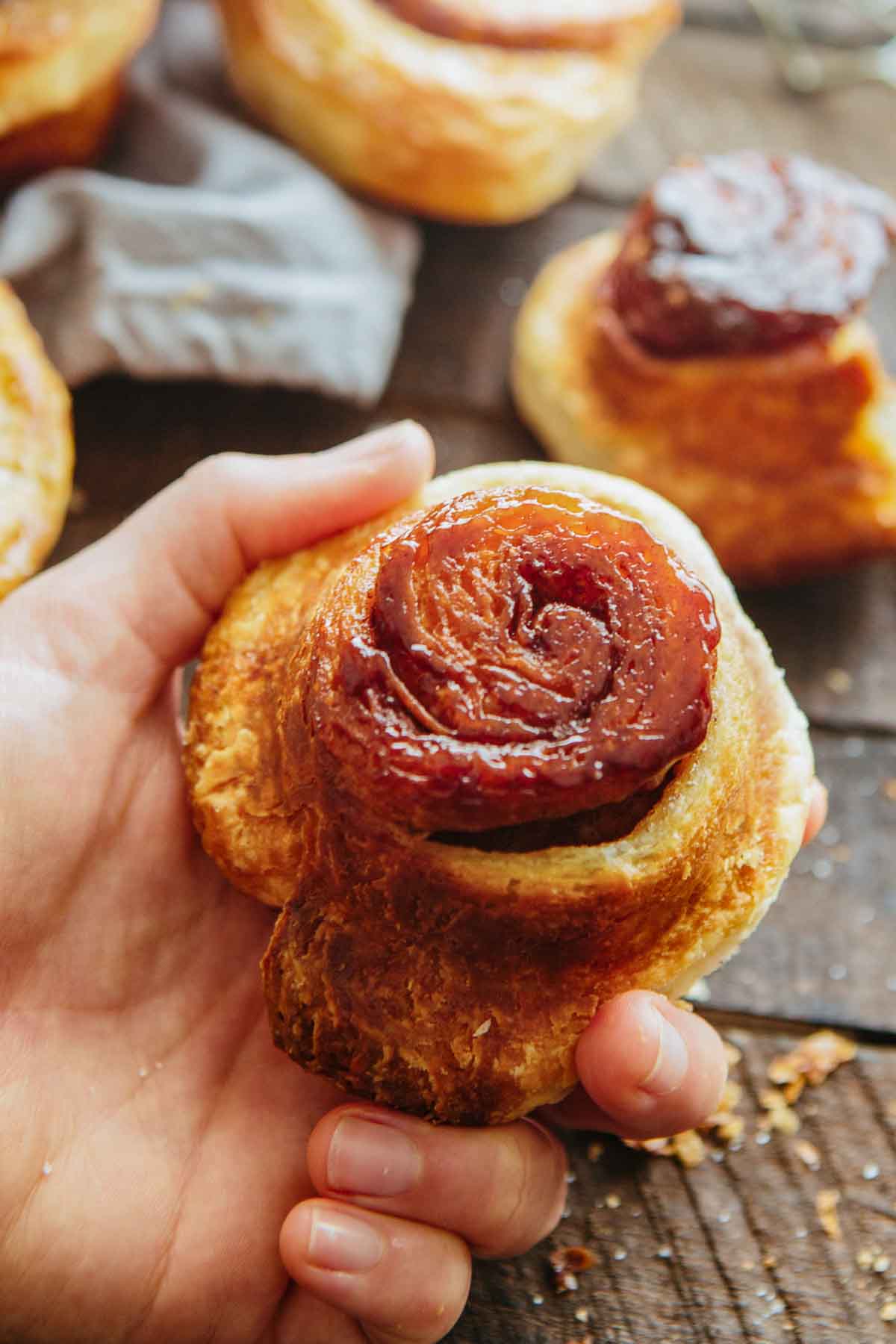 A hand holding a morning bun with a caramelized bottom, showing glossy sticky caramel and flaky pastry edges.