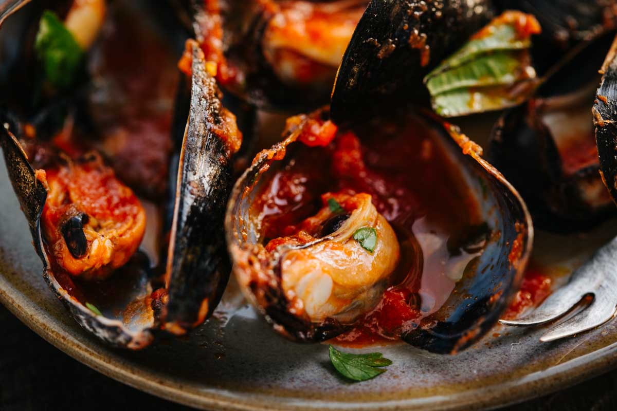 A close look at opened mussels in tomato broth on a plate, highlighting the tender meat and herbs.