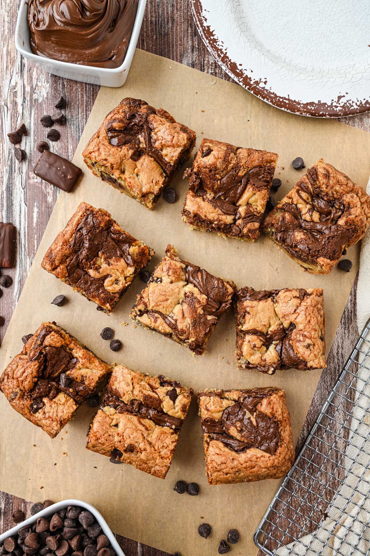 Squares of baked Nutella blondies arranged on parchment with chocolate chips and toffee pieces scattered around.