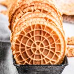 A tight row of golden pizzelles standing upright in a patterned metal tin.