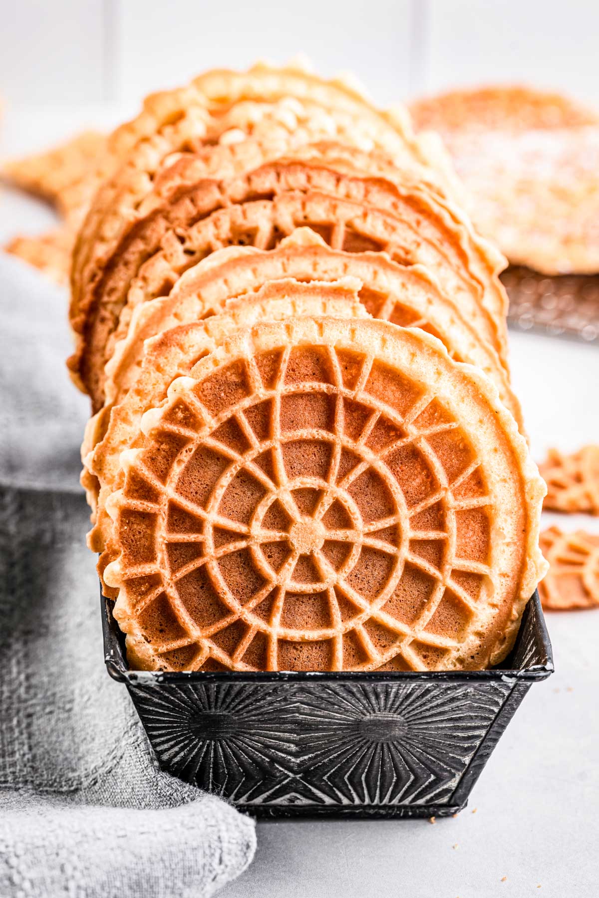 A tight row of golden pizzelles standing upright in a patterned metal tin.