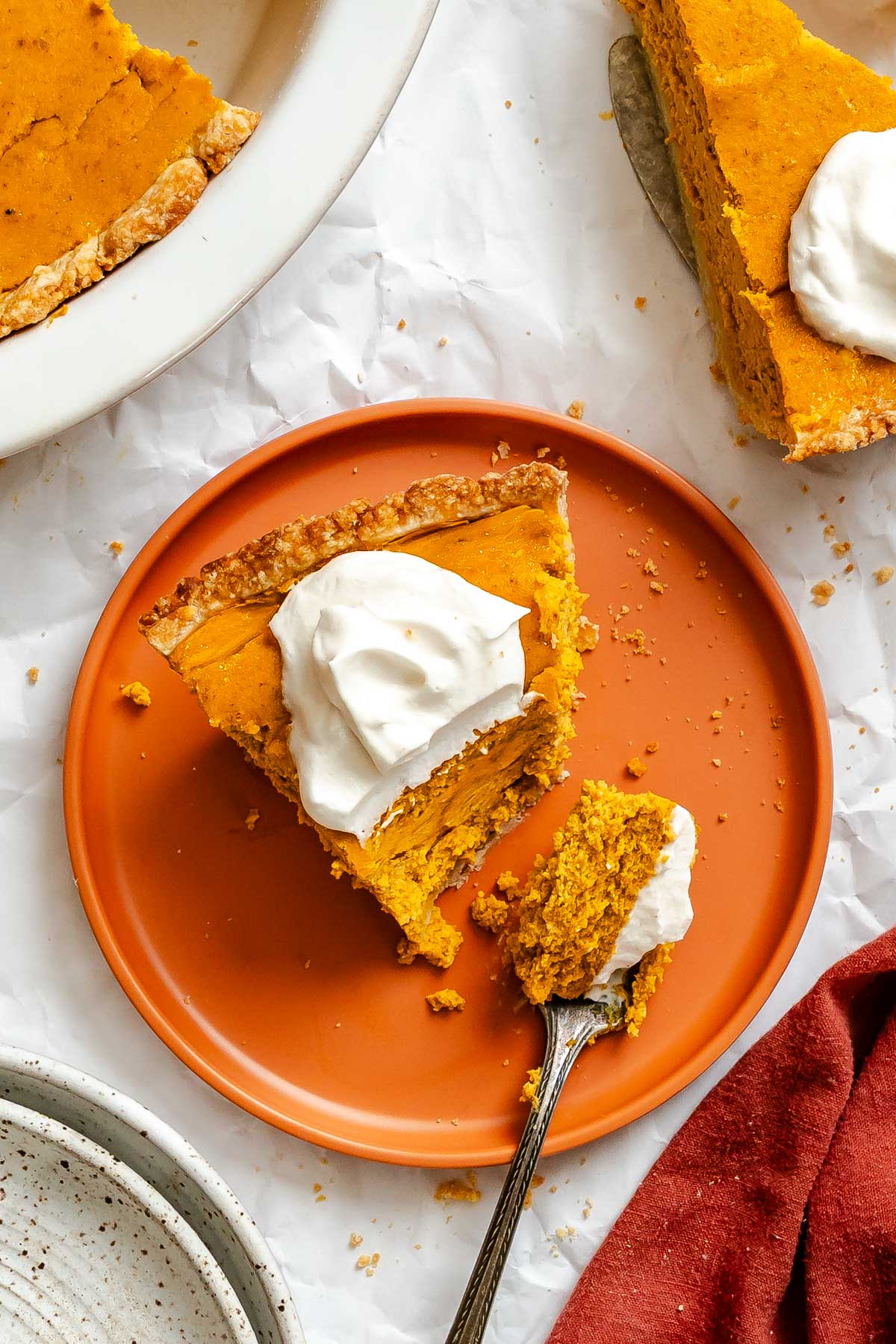 Top view of a slice of pumpkin ricotta pie on an orange plate, a bite taken with a fork, showing the smooth, custardy filling.