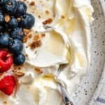 Close-up of creamy strained Greek yogurt topped with blueberries, raspberries, and granola.