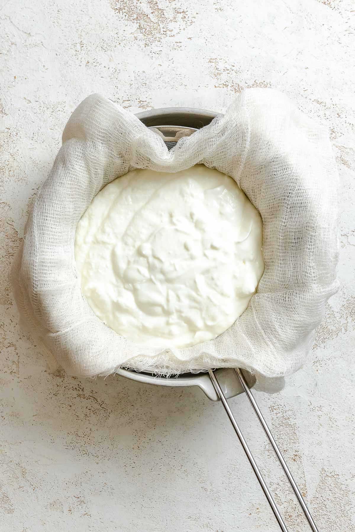 Strainer lined with cheesecloth filled with yogurt, ready to be strained.