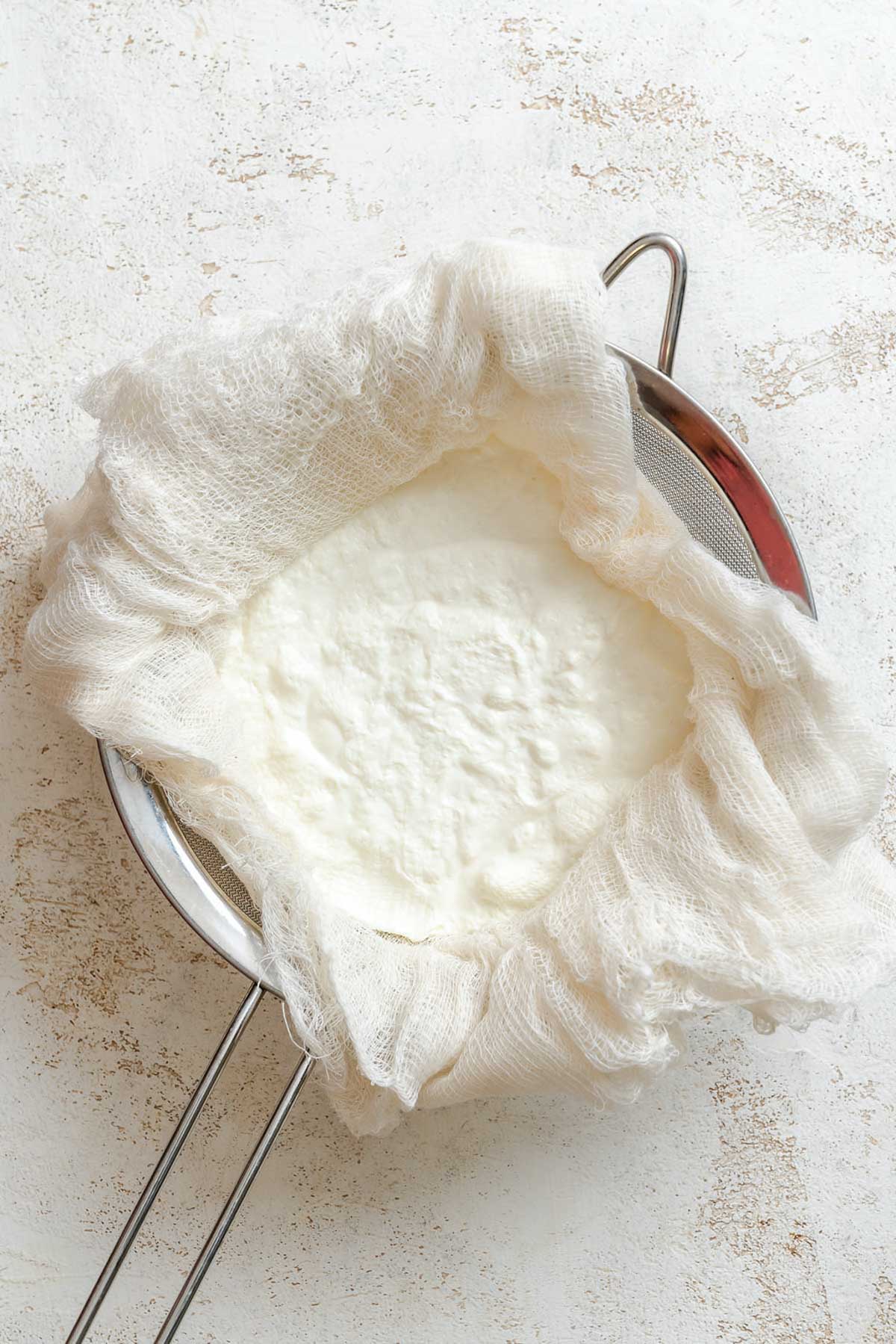 Yogurt beginning to thicken inside cheesecloth as whey drains out.