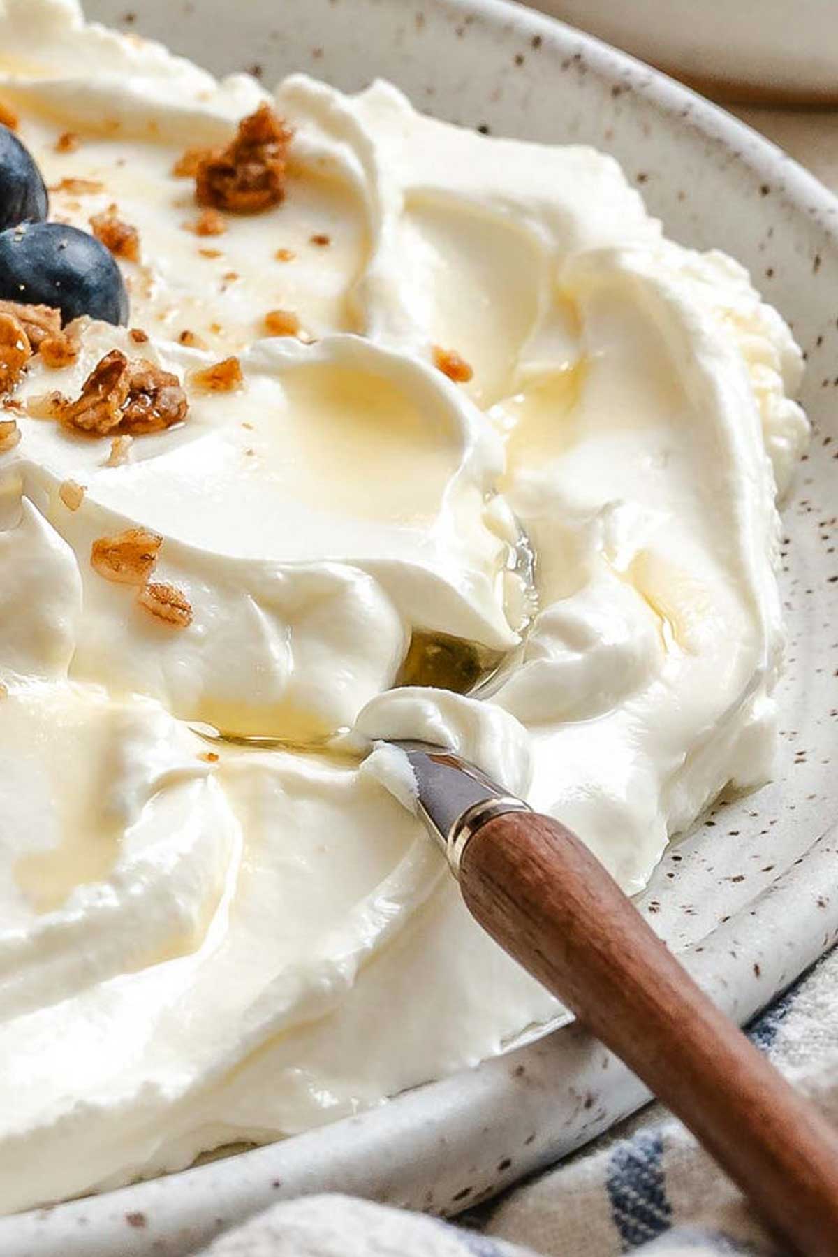 Close-up of smooth, thick Greek yogurt with a small spoon and honey drizzle.