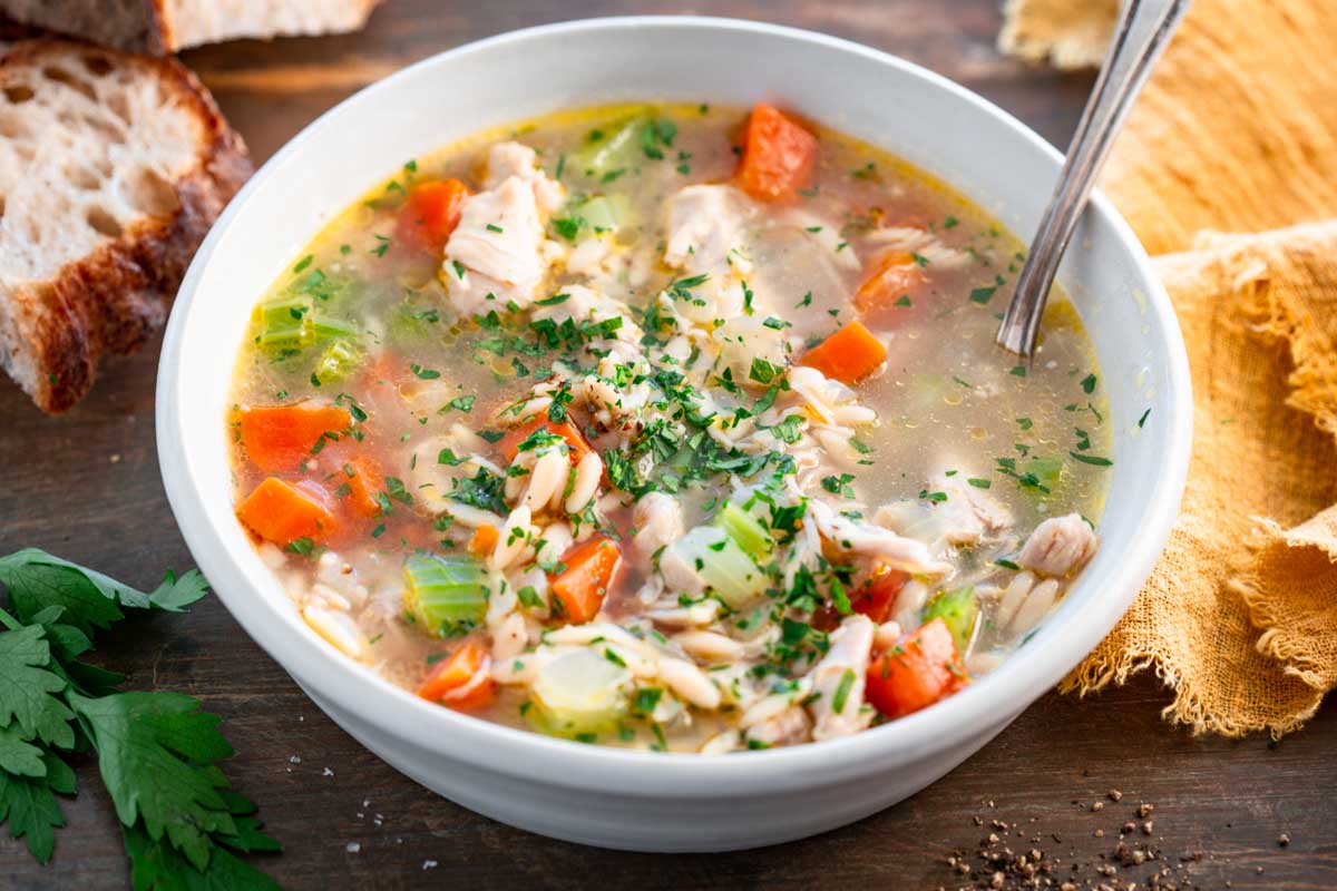 Close-up of turkey orzo soup showing vegetables, shredded turkey and chopped parsley.