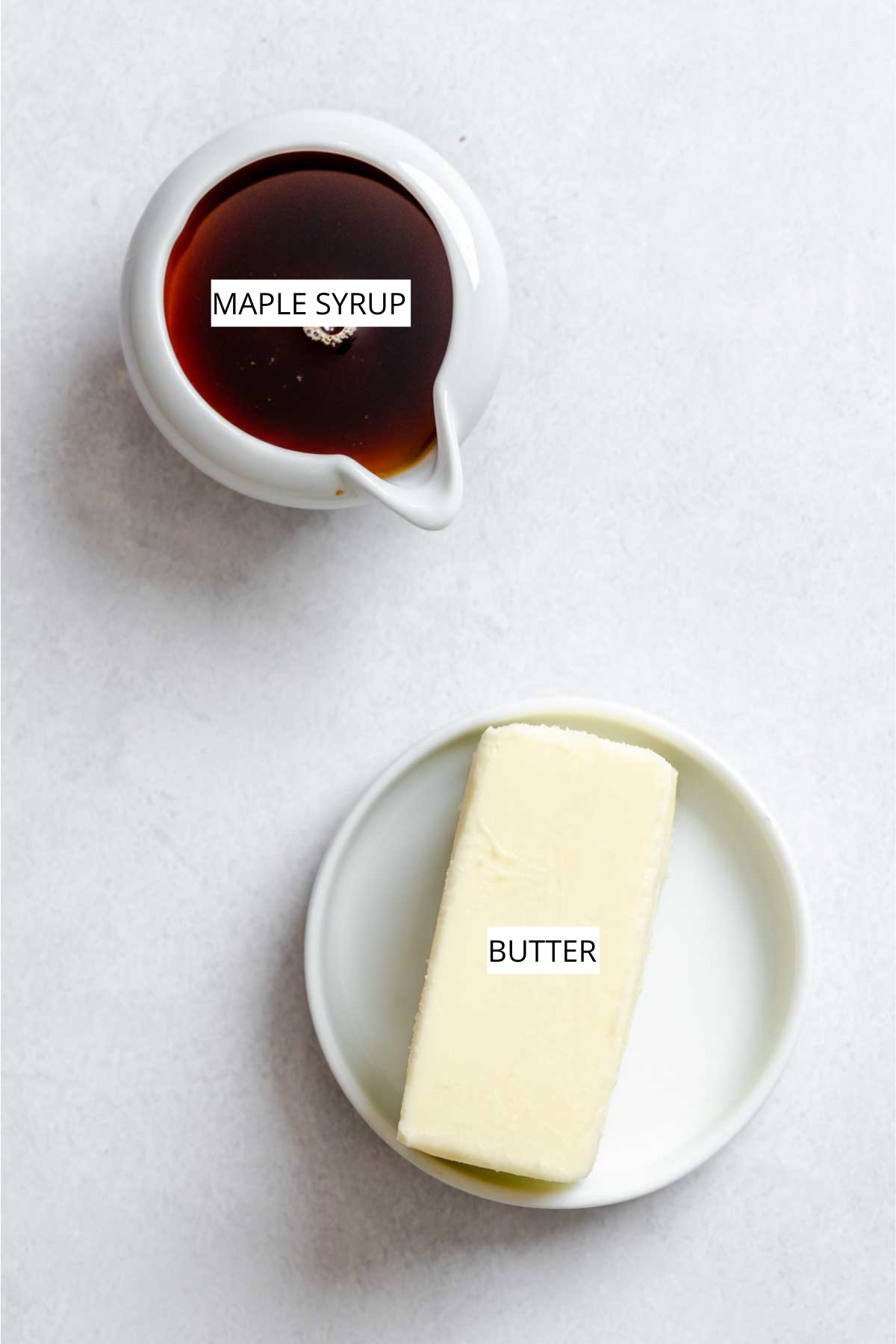Pure maple syrup in a small white pitcher and a stick of butter on a white plate, photographed from overhead on a light background.