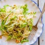 A plate of celery root and pear salad with frisee, walnuts and manchego seen from above on a rustic wooden table.