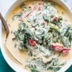 Bowl of lighter creamed spinach made with Greek yogurt, showing a smooth, creamy sauce and wilted spinach, styled on a green napkin.