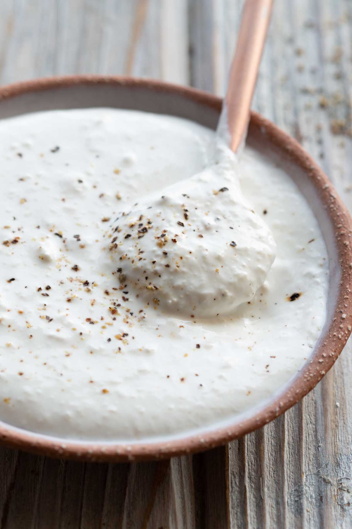 A spoon lifting a dollop of thick horseradish sauce from a small bowl, showing its creamy texture.