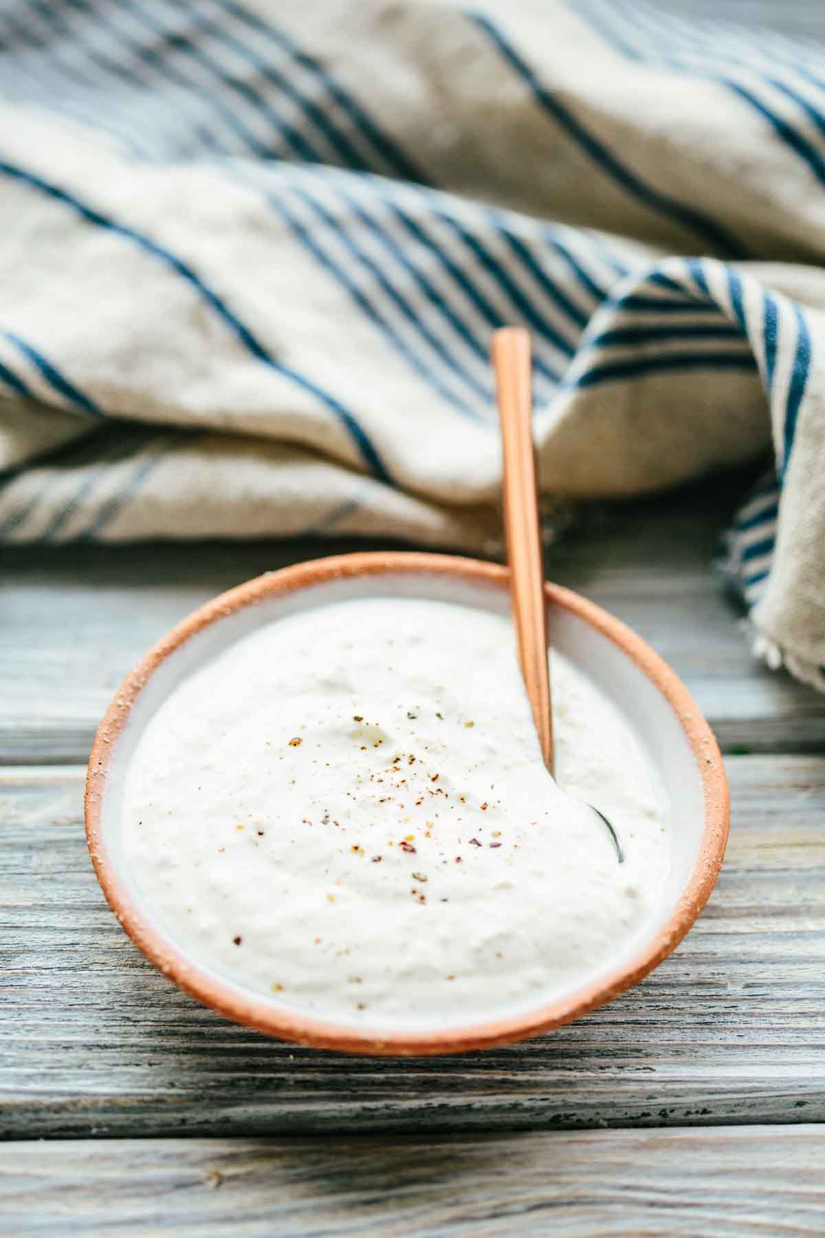 A bowl of creamy horseradish sauce topped with pepper, placed in front of a striped kitchen towel.