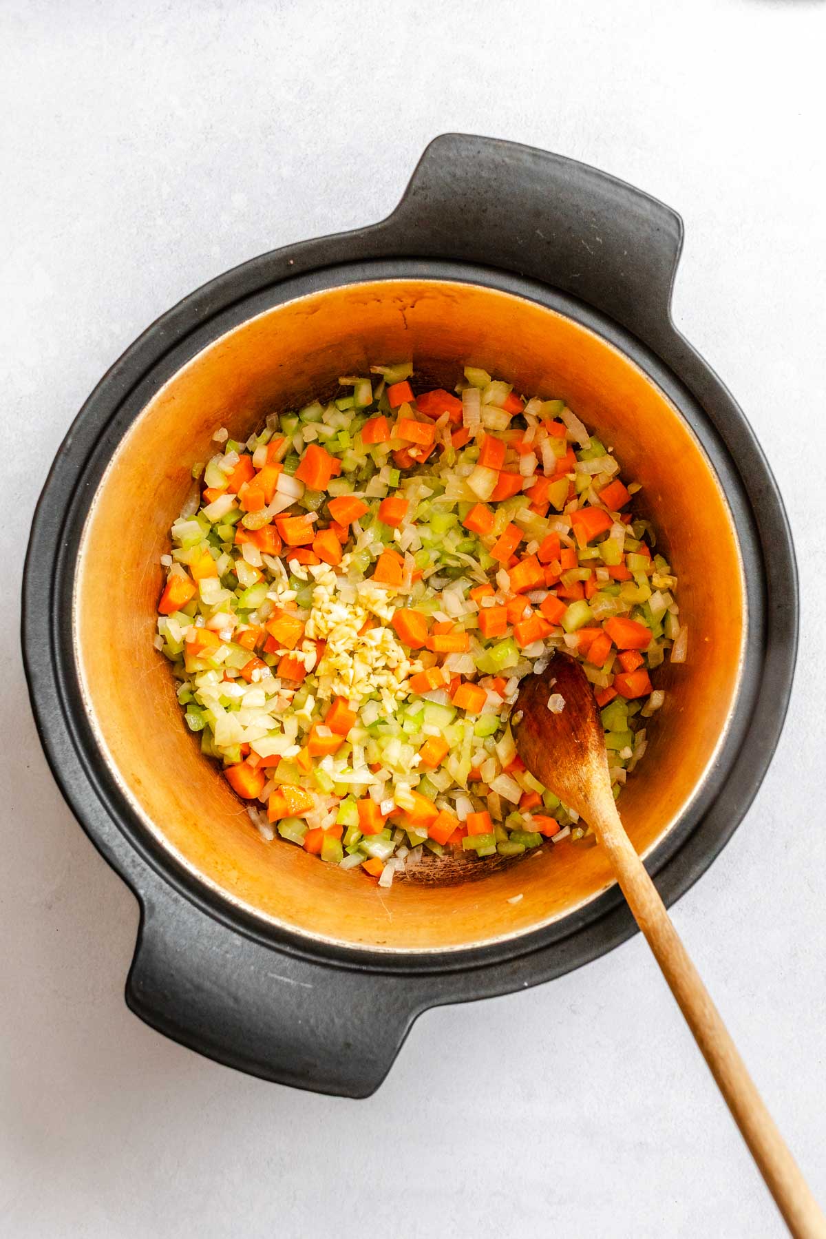Sautéed onions, carrots and celery in a Dutch oven with freshly added minced garlic in the center.