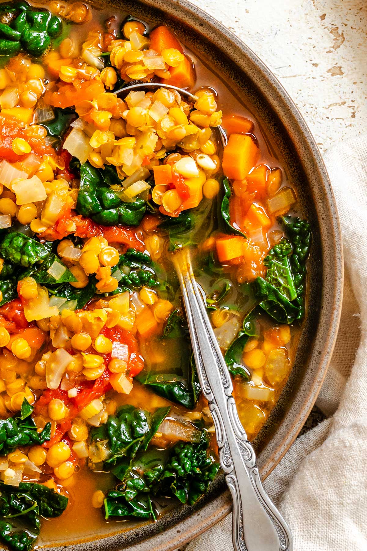 A close look at cooked lentils, tomatoes and kale in broth, showing tender vegetables and rich color.