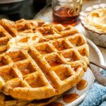 Close-up of oatmeal waffles showing crisp edges and syrup pooling in the waffle pockets.