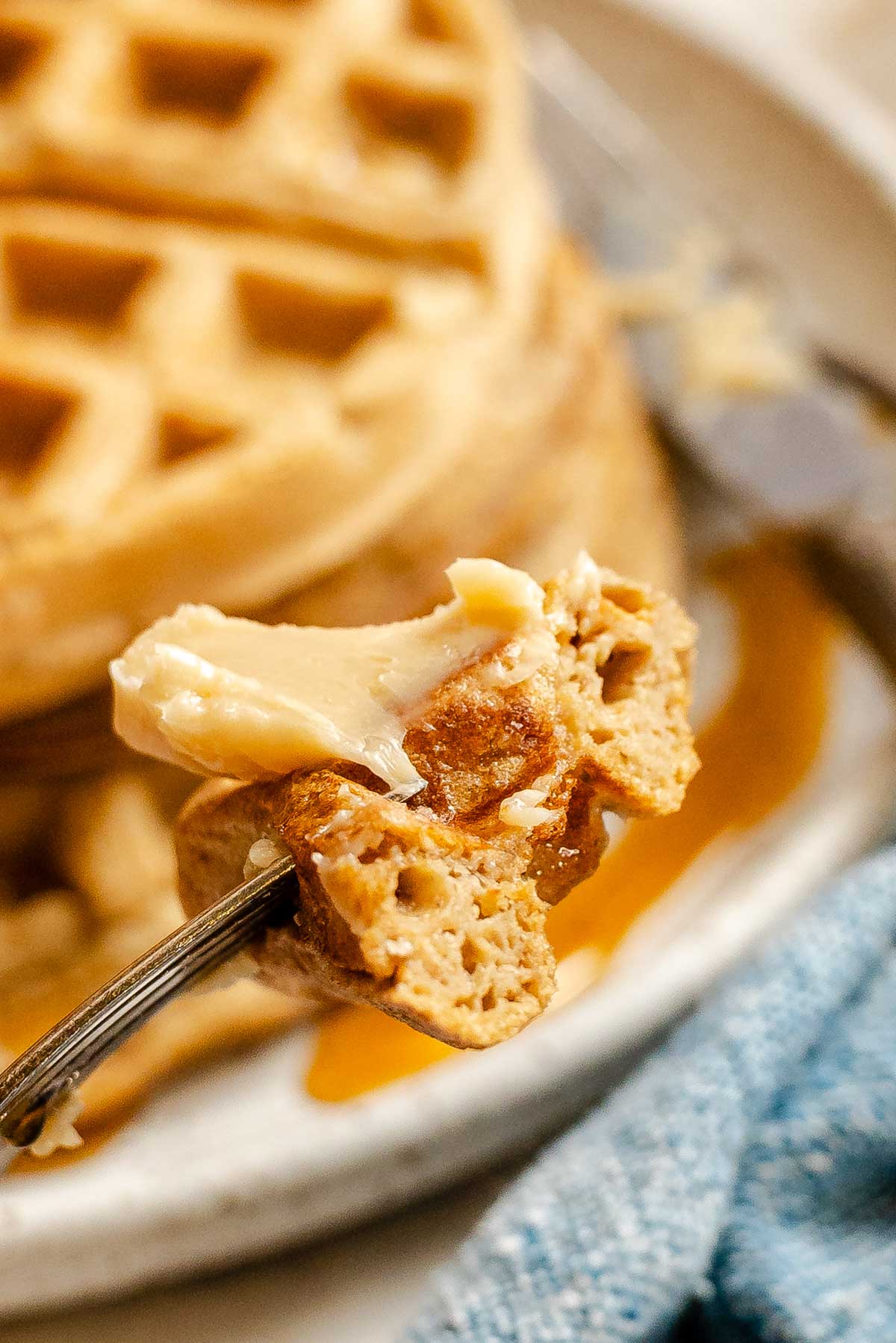 Fork holding a bite of oatmeal waffle with melted butter and maple syrup, showing the tender interior texture.