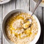 A shallow bowl filled with creamy pastina topped with grated Parmesan, cracked black pepper and a drizzle of olive oil, with a spoon scooping up a bite.