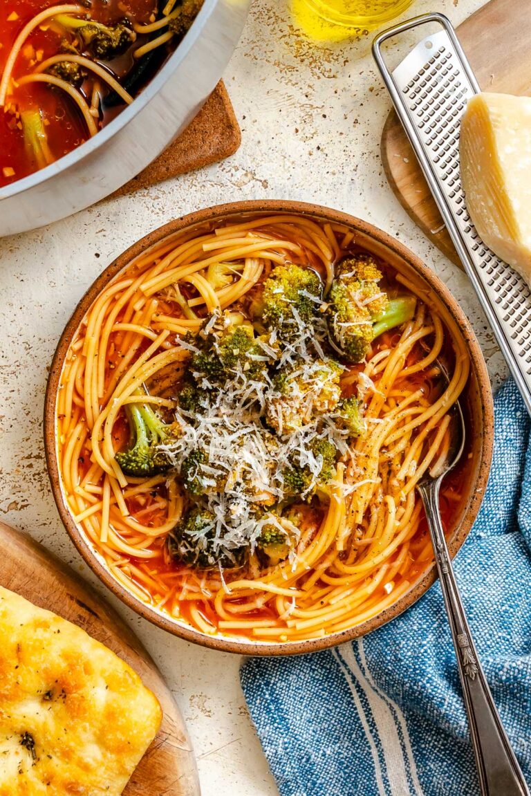 Finished Sicilian broccoli soup with pasta and broccoli ready to serve, with olive oil, bread, and cheese nearby.