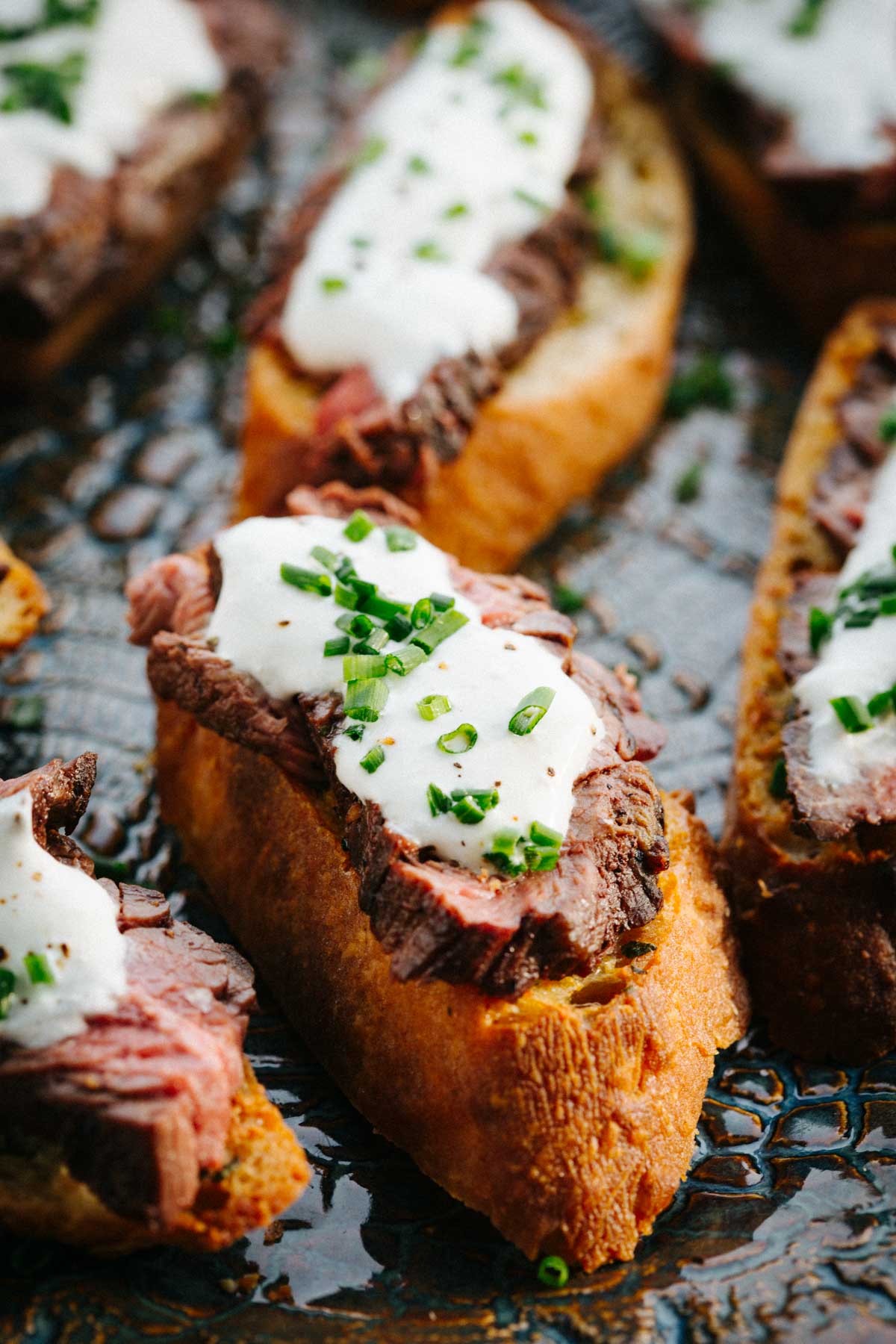 A close view of a single crostini showing the seared steak, creamy sauce and bright green chives on crisp toasted bread.