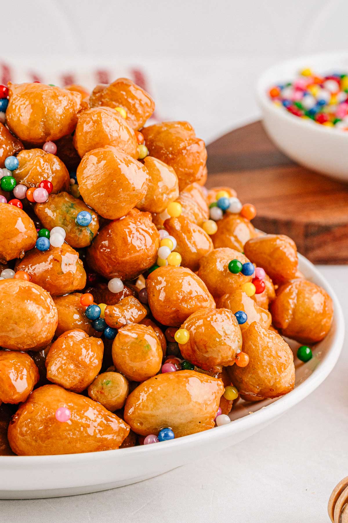 A close up shot showing the glossy fried dough balls coated in honey with bright sprinkles nestled between them.