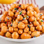 A side angle of the full platter of honey coated struffoli emphasizing their shape, shine and colorful decorations.