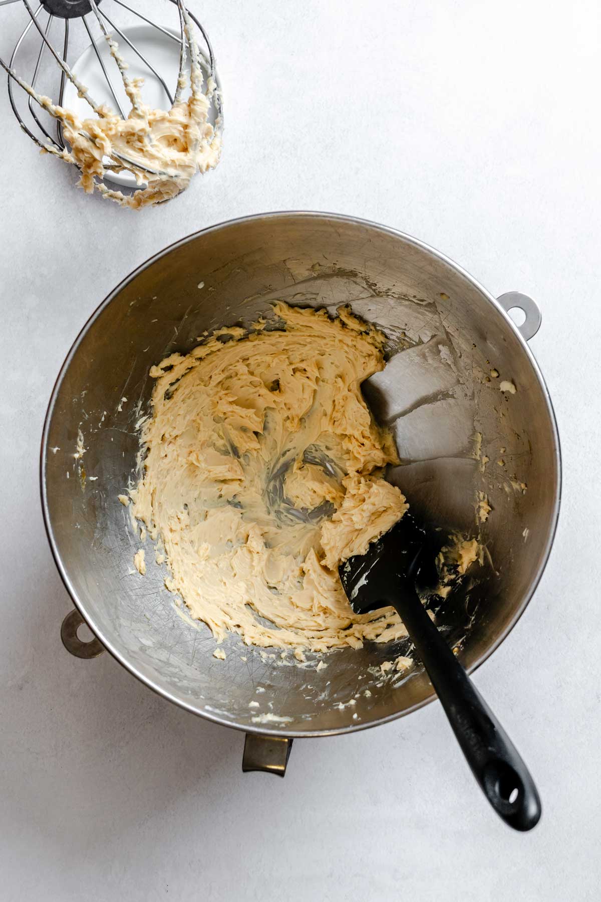 Maple butter whipped to a pale, creamy texture inside a metal mixing bowl with a rubber spatula resting inside.