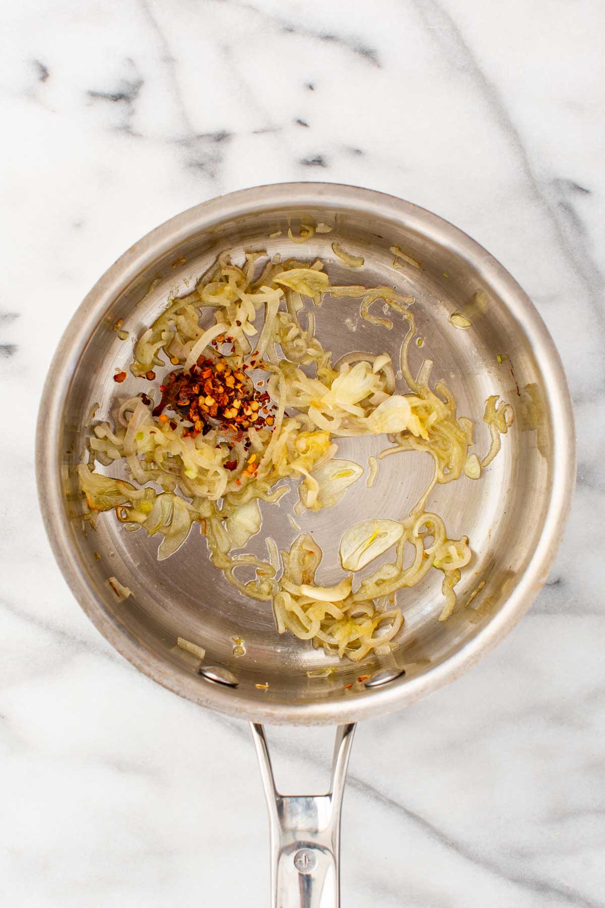 Thinly sliced shallots and garlic cooking in a saucepan with olive oil and red chili flakes until soft and translucent.