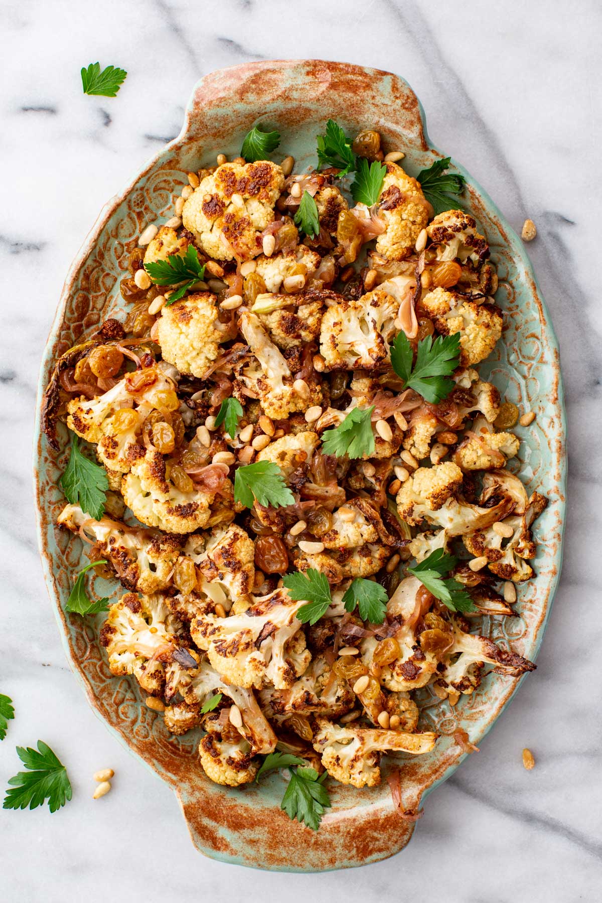 Roasted cauliflower agrodolce tossed with raisins, pine nuts, and parsley, arranged on a serving platter.