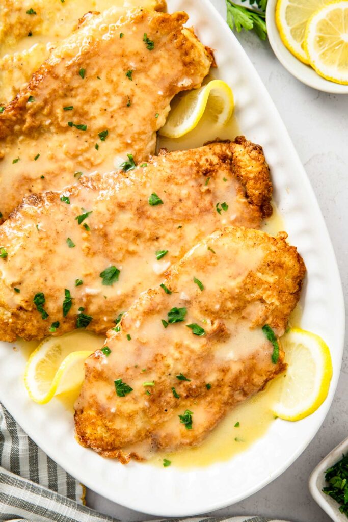 Close up of chicken francaise showing the golden crust coated in glossy lemon butter sauce with parsley scattered on top.
