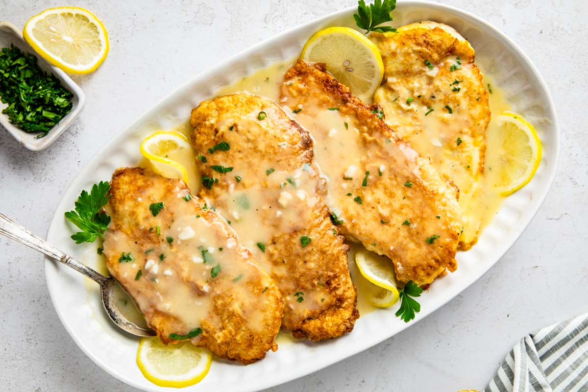 Plated serving of chicken francaise with lemon slices and extra sauce pooled on the plate.