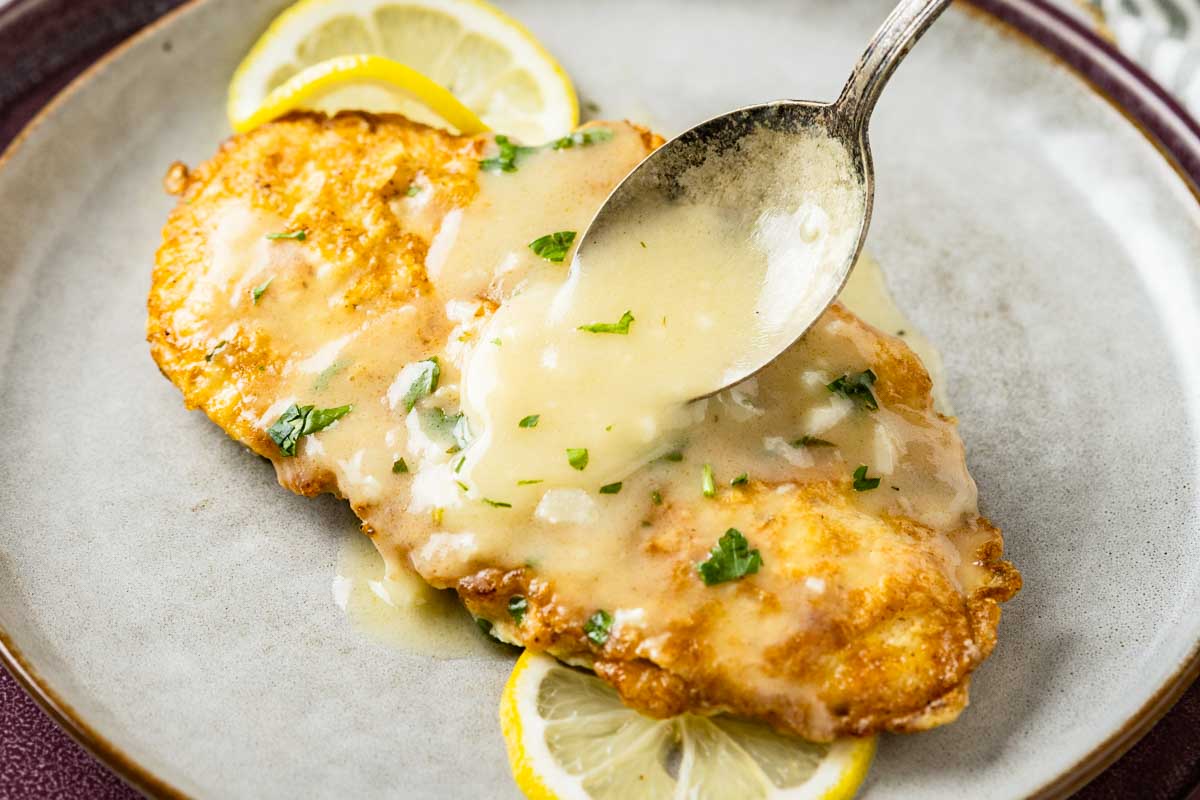 Close up of lemon butter sauce being spooned over a piece of chicken francaise, showing the creamy texture of the sauce.