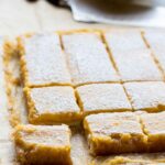 Angled view of grapefruit bars cut into squares and resting on parchment paper, lightly dusted with powdered sugar.