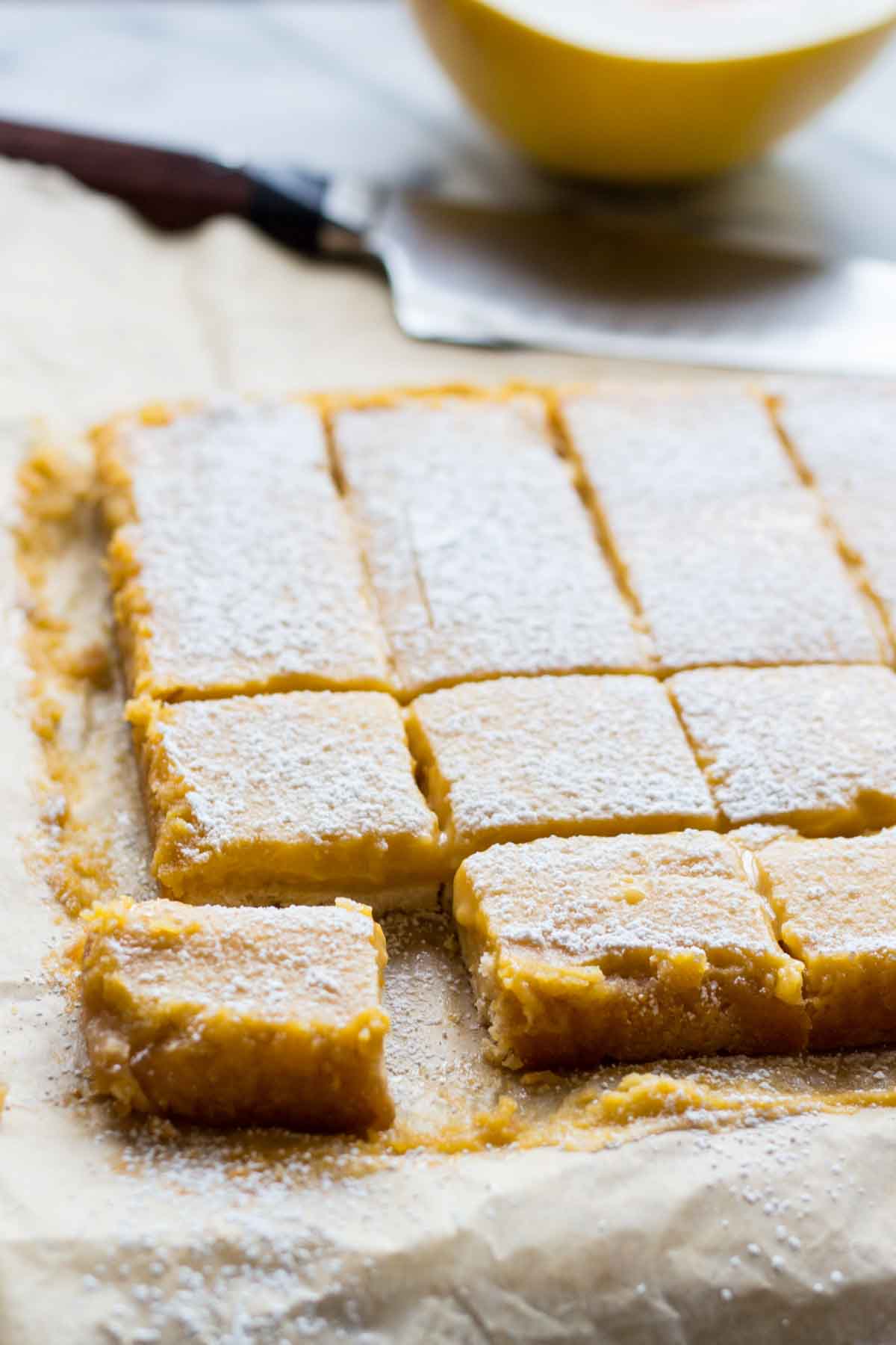 Angled view of grapefruit bars cut into squares and resting on parchment paper, lightly dusted with powdered sugar.