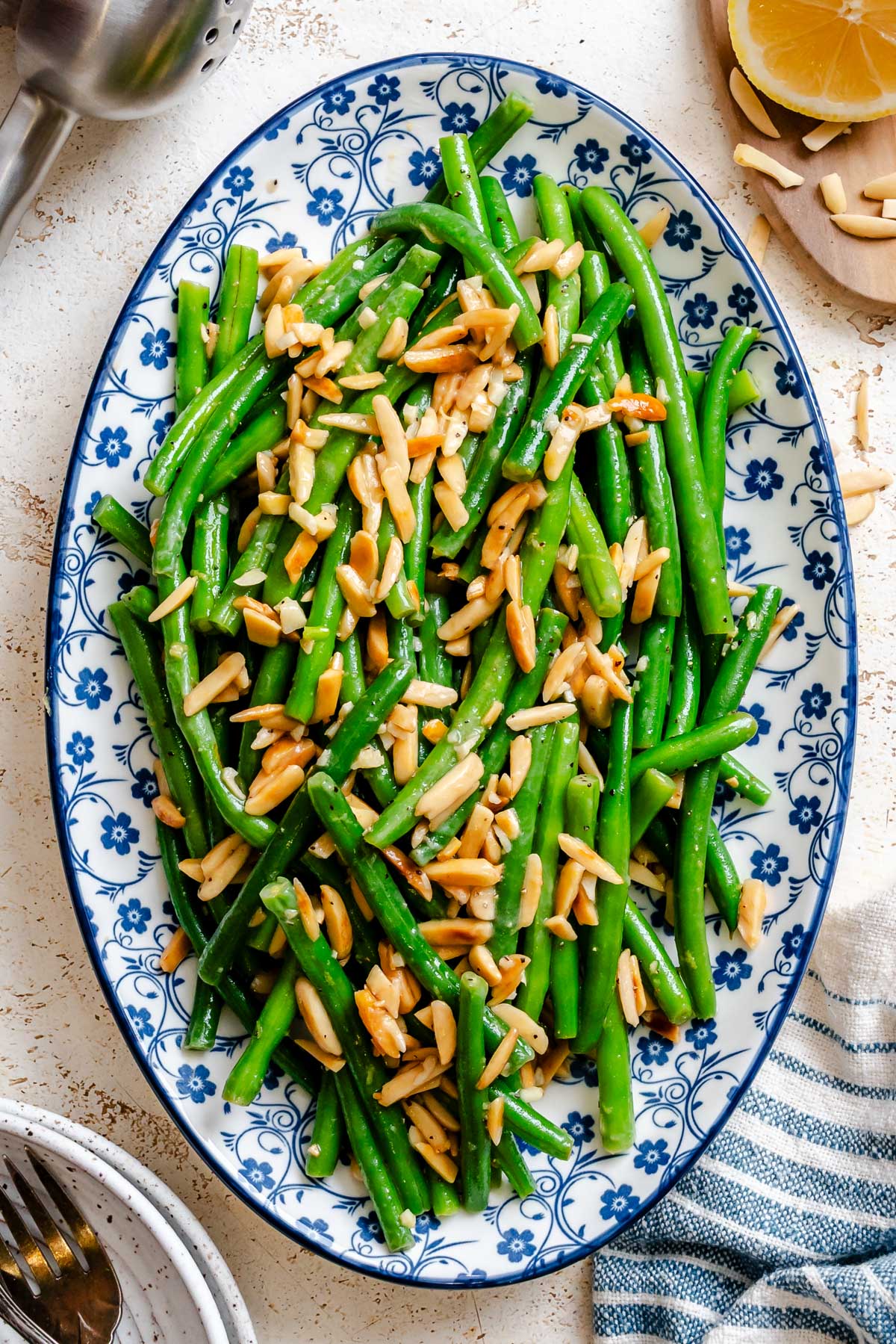 Overhead view of green beans amandine arranged on a patterned serving platter, with golden toasted almonds scattered throughout.