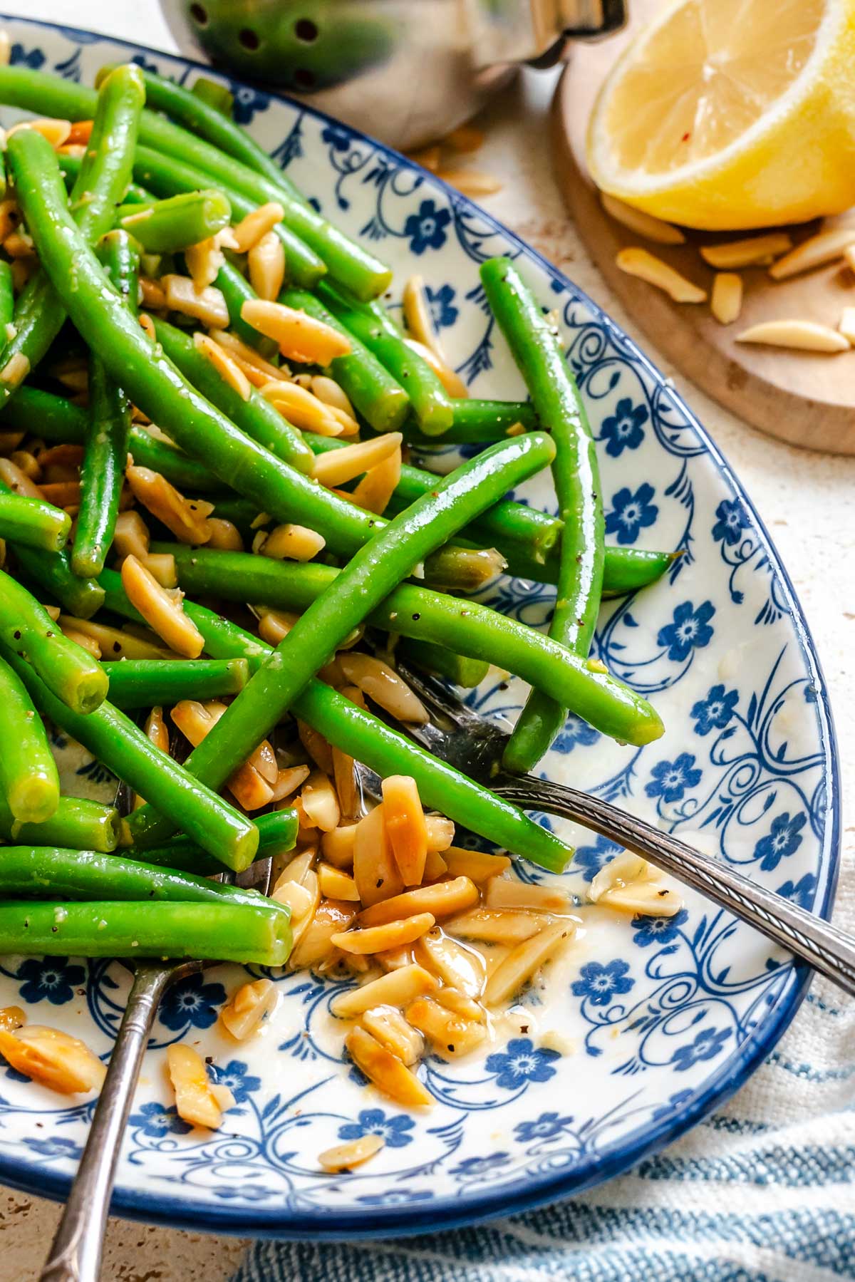 Close up of green beans amandine with a fork lifting a bite, showing the buttery sauce pooling with toasted almonds.