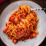 Close up of lobster fra diavolo as a fork lifts strands of spaghetti coated in tomato sauce with visible pieces of lobster.