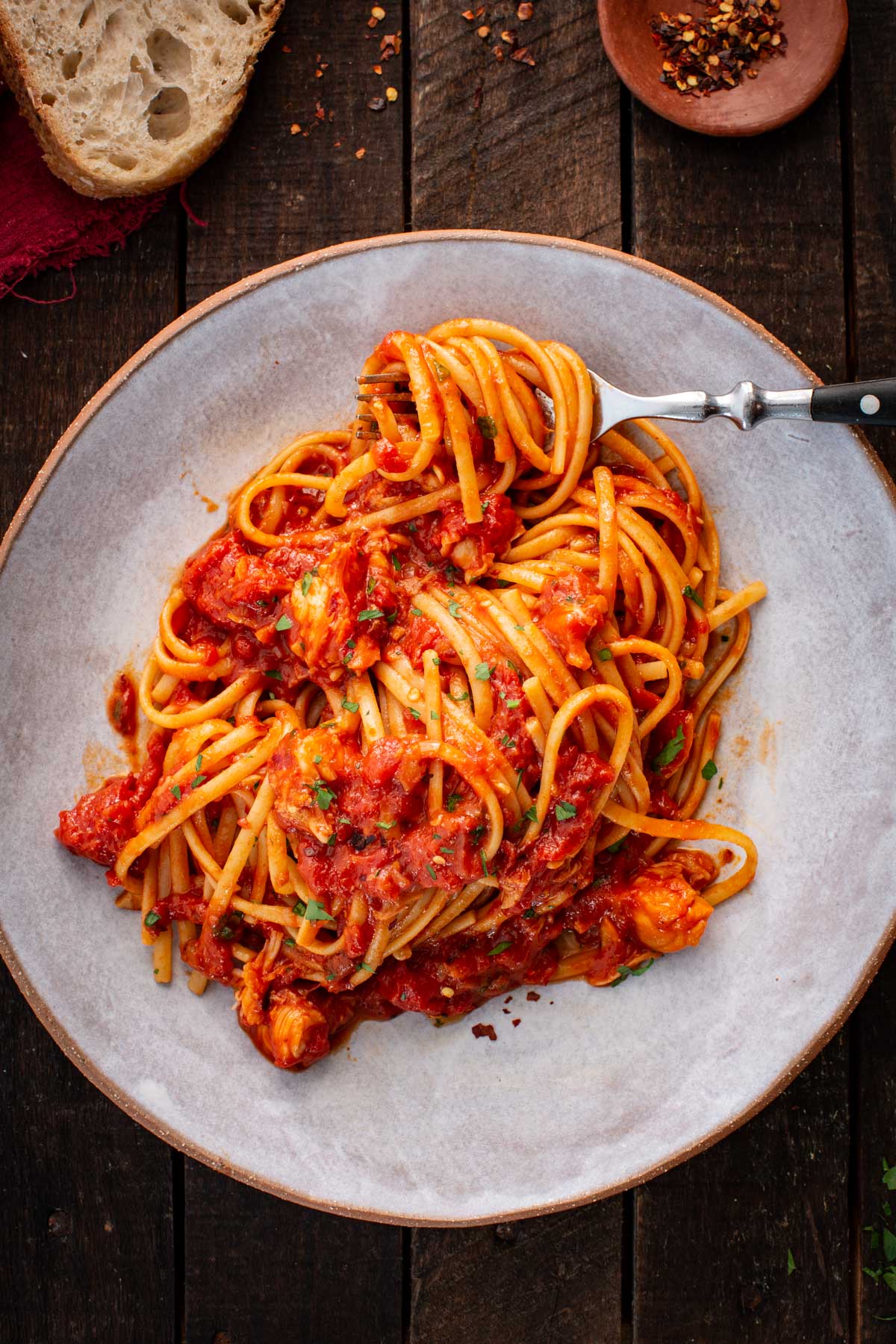 Close up of lobster fra diavolo as a fork lifts strands of spaghetti coated in tomato sauce with visible pieces of lobster.