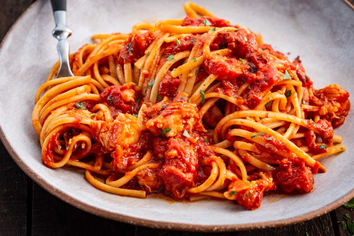 Tight close up of spaghetti and lobster tossed in a thick tomato fra diavolo sauce, showing the texture of the pasta and lobster meat.