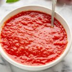 Vibrant tomato sauce in a white bowl with a spoon dipped in.