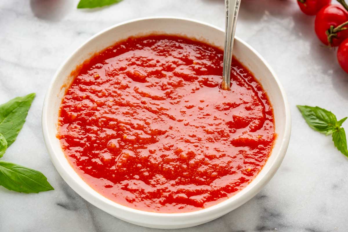 Vibrant tomato sauce in a white bowl with a spoon dipped in.