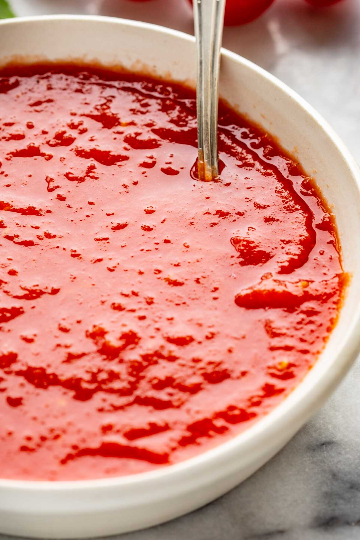 Close-up view of pizza sauce in a white bowl showing a slightly chunky, glossy texture.