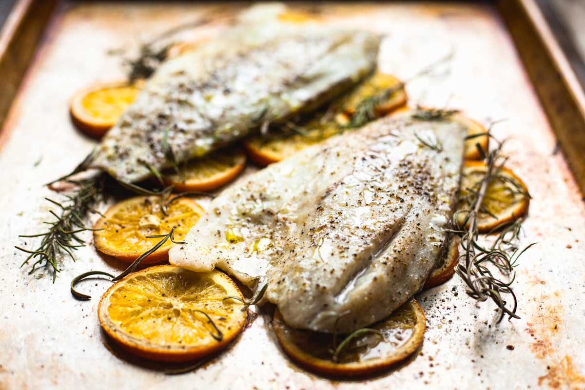 White fish fillets roasted on a sheet pan over sliced oranges with fresh rosemary, olive oil, salt and black pepper.