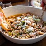 Overhead view of the finished stew showing tender beans, wilted escarole, and sausage in broth.